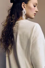 Remera de algodón color crema, corte oversized con hombros caídos y cuello redondo. Presenta un estampado frontal en negro de un pájaro (golondrina) sobre una cinta con el texto "COME UNDONE" y "Wuthering Heights".