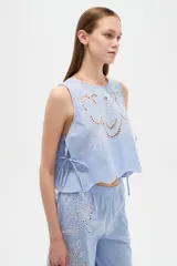 Musculosa de algodón color celeste, con cuello redondo y detalles bordados en tono blanco con diseño de broderie en la parte frontal. Cuenta con cordones laterales para ajustar.