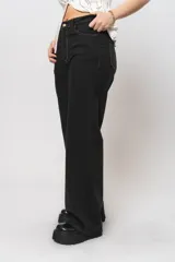 Pantalón jean negro de corte wide leg con costuras en tono beige y tela alicrada.