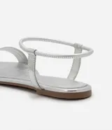 Sandalias planas blancas con tira elástica en el tobillo y tira fija sobre los dedos.