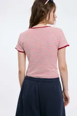Remera baby blanca de algodón, de corte cropped al cuerpo y mangas cortas. Presenta ribetes negros en contraste en el cuello redondo y los puños, con un estampado localizado de un ají rojo con la inscripción 'Pimentón' en el centro del pecho.