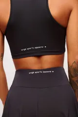 Top deportivo negro, estilo crop top, con cuello polo y escote en V. Presenta tirantes anchos y corte ajustado al cuerpo.