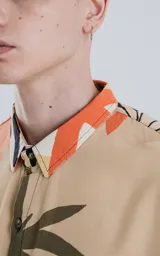 Camisa de manga larga con cuello y botones frontales, confeccionada en rayón con un estampado de hojas tropicales en tonos beige, naranja, negro y verde oliva.