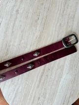 Cinturón de cuero vacuno color bordó con apliques metálicos en forma de rombo y hebilla cuadrada de metal envejecido.
