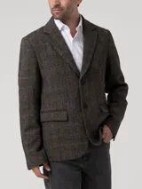 Blazer de lana Harris Tweed con patrón de espiga y cuadros sutiles en tonos tierra, azul y naranja. Presenta cierre frontal de dos botones, solapas clásicas y bolsillos con solapa. Incluye forro interior satinado.