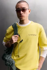 Camiseta de corte relaxed fit color amarillo, confeccionada en tejido compacto de algodón, con cuello redondo, manga corta y estampado frontal a contraste con texto y motivo floral pequeño.
