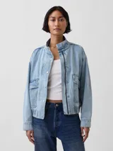 Campera bomber de jean con lavado claro, cuello alto con botones a presión, cierre frontal, bolsillos con solapa en el pecho y elástico en el dobladillo inferior y los puños.