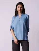 Blusa de lyocell color azul claro, con cuello camisero, escote en V con tapeta de botones y mangas largas con presilla para regular el largo.