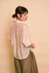 Camisa de manga corta color beige, translúcida, con cuello camisero, cierre frontal con botones y bordados florales tono sobre tono.