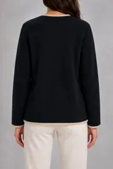 Saco de punto negro con diseño cruzado, cuello en V y ribetes en color beige. Presenta cierre frontal con botones claros, dos bolsillos delanteros aplicados y mangas largas.