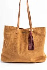 Bolso tipo tote de gran tamaño confeccionado en gamuza sintética color tostado. Presenta un diseño minimalista con asas largas de hombro y una pequeña placa metálica frontal con el logo de la marca.