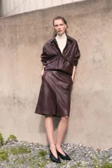 Pollera tubo de cuero sintético color marrón oscuro, de largo hasta la rodilla, con tajo frontal y cierre oculto en la parte trasera.