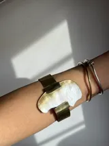 Brazalete rígido hecho a mano en bronce dorado con pieza irregular de nácar engarzada.