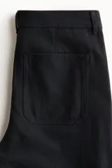 Pantalón amplio de sarga de algodón negro, con perneras rectas, bolsillos delanteros de parche y cierre frontal con botón.