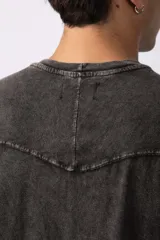 Remera de corte oversize con efecto de lavado gastado, confeccionada en algodón pesado. Presenta cuello redondo, mangas cortas con costuras visibles y un diseño amplio.