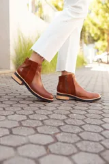 Botas tipo Chelsea de cuero, con diseño de paneles combinados en texturas lisas, gamuzadas y con relieve tipo reptil en el talón. Presentan una suela plana con taco bajo de madera y base de goma negra.