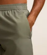 Bermuda deportiva masculina color verde oliva, confeccionada en poliéster y elastano. Posee cintura elástica con cordón interno ajustable y estampa reflectante en el lateral. Ideal para actividades deportivas.