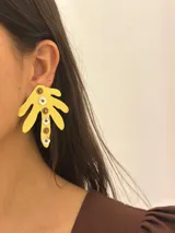 Aros colgantes con forma de hoja de palma color amarillo y apliques circulares en tonos marrón y blanco.