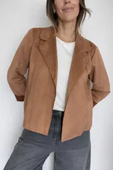 Chaqueta corta de diseño abierto con textura efecto ante, de corte recto y estilo liviano. Presenta solapas clásicas y mangas largas con puños vueltos en un tono más oscuro.