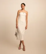 Vestido midi blanco sin breteles, confeccionado en bengalina. Presenta detalle de hebilla plateada en el busto y abertura en la parte trasera.