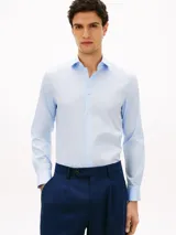 Camisa celeste de corte slim, confeccionada en sarga de mezcla de algodón elástico. Cuenta con cuello italiano, manga larga con puños y cierre frontal con botones.