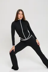Conjunto deportivo de tres piezas compuesto por un top con breteles finos, una campera entallada con cierre frontal y una calza semioxford. Todas las prendas son de color negro con detalles de ribetes blancos en los bordes.