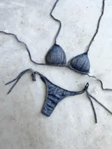 Bikini de dos piezas color azul con estampado a cuadros. El top es de triángulos movibles con tiras para atar al cuello y espalda, e incluye almohadillas desmontables. El bottom es colaless con tiras para atar en los laterales.