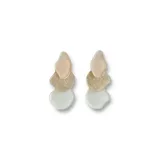 Par de aros colgantes con tres piezas irregulares superpuestas: una superior color piel, una intermedia dorada con textura brillante y una inferior color blanco hueso.