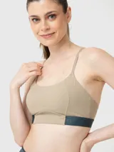 Top deportivo de sujeción media y corte ajustado, color beige con banda inferior bicolor en azul oscuro. Confeccionado con tecnología Aloe Vera.