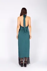 Vestido largo verde petróleo de seda lavada, con escote halter cruzado, abertura en el abdomen, falda con capas y flecos.
