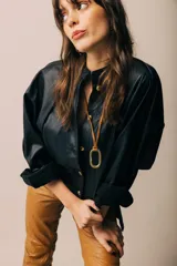 Collar con dije ovalado de bronce colgando de un tiento de cuero marrón.