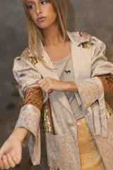 Blazer de corte recto con diseño combinado en brocato y lentejuelas doradas. Presenta mangas con volumen en los hombros y puños largos con recortes geométricos en cuero marrón.