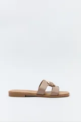 Sandalias planas marrones con capellada de dos tiras cruzadas y hebilla metálica decorativa.