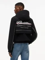Cortavientos negro con capucha fija, cierre frontal de cremallera con cinta distintiva y puños elásticos. Presenta logos de la colaboración Cadillac Formula 1 Team en el pecho y diseño de corte regular.