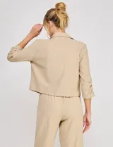 Blazer corto de lino color beige, marca Allie Rose, de estilo relajado y corte crop con frente abierto sin botones. Presenta solapa de muesca y mangas tres cuartos con detalle fruncido en los laterales.