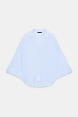 Camisa de mujer color celeste con finas rayas verticales blancas. Presenta un corte amplio y holgado, cuello solapa con escote en pico y mangas anchas que terminan en puño. Cierre frontal con botones.