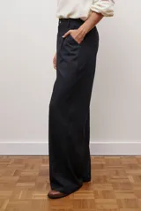 Pantalon de corte recto y pierna ancha, confeccionado en tejido tipo denim oscuro. Presenta tiro alto, cintura con cierre frontal y bolsillos laterales funcionales.