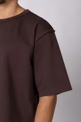 Remera de corte oversize color beige, con cuello redondo y etiqueta decorativa pequeña en el ruedo inferior.
