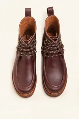 Bota de cuero vacuno color bordó con acabado charol, diseño de caña media con cordones y ganchos metálicos. Presenta costuras visibles en la puntera y suela de goma tipo crepe.