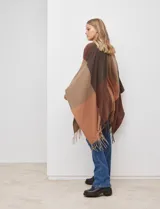 Ruana tejida con diseño colorblock en tonos de gris y beige, con flecos en el borde inferior.