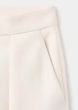 Pantalón de vestir color crudo, de corte recto y largo, con pliegues en los laterales y cierre delantero de cremallera metálica expuesta.