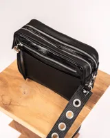 Bandolera negra de charol con doble compartimento, bolsillo frontal, correa regulable con ojalillos y detalles metálicos plateados.