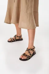 Sandalias de cuero color beige, con tiras cruzadas en el empeine decoradas con tachas y esferas doradas, base anatómica y pulsera ajustable al tobillo.