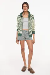 Campera de punto de algodón y acrílico, con diseño geométrico radial en tonos verdes y blanco, cuello alto y cierre frontal completo.