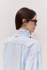 Camisa celeste con cuello alto, volados frontales y mangas largas con puños ajustados.