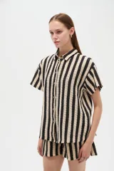 Camisa de algodón de corte holgado, con diseño de rayas verticales en colores negro y beige, cuello camisero y cierre frontal con botones.