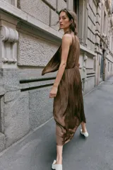 Vestido midi satinado de color marrón, con cuello fluido y diseño sin mangas. Presenta un cierre en la espalda con botones y una falda fluida con sutiles pliegues.