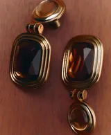 Pendientes colgantes dorados con diseño articulado, compuesto por una pieza superior circular abombada y un colgante rectangular inferior con una piedra de cristal marrón facetada y marco texturizado con líneas concéntricas.