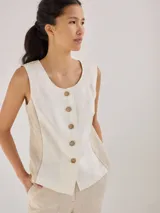 Chaleco sin mangas de lino, con diseño de paneles en color blanco crudo y beige. Presenta escote redondo y cierre frontal con botones de madera marrones.