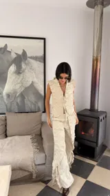 Pantalón de lino color beige con diseño de tablas verticales aplicadas que aportan textura y movimiento. Presenta tajos laterales, bolsillos delanteros y traseros, y un corte holgado.